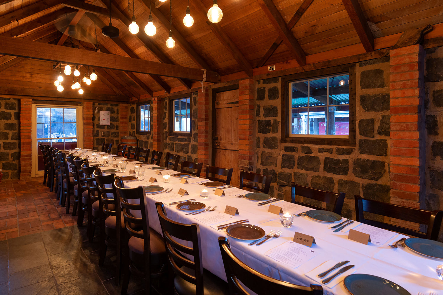 Long dining table set for a meal in the Bluestone Cottage, a rustic stone-walled room with wooden beams.
