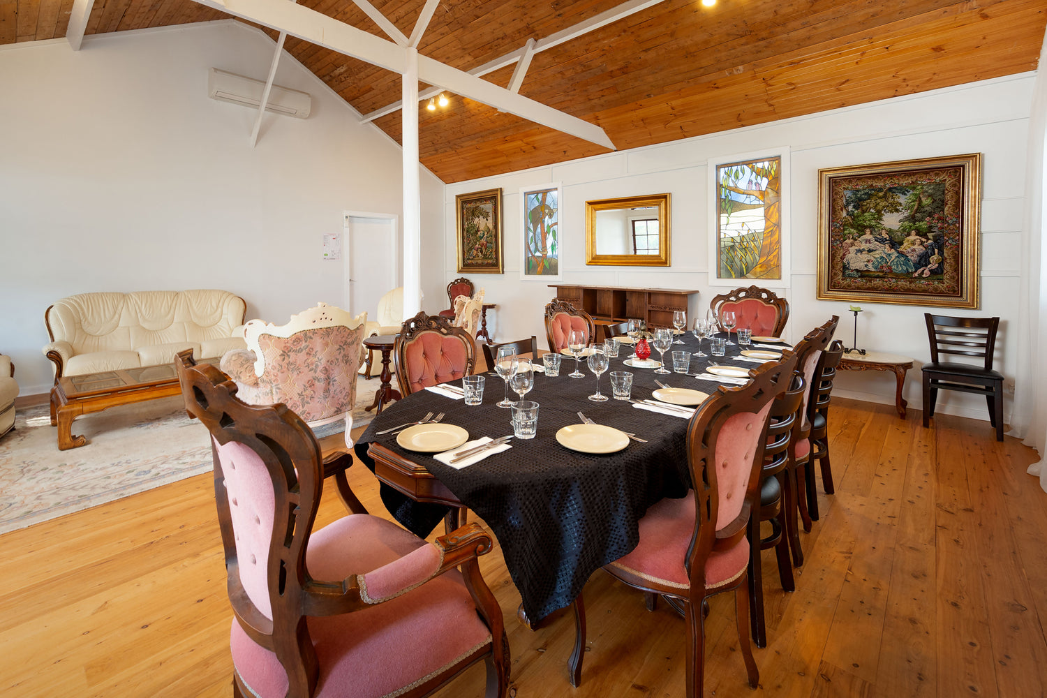Executive Cottage with wooden floor, pink velvet dining chairs at a long oval table, vaulted ceiling, and framed artwork on the walls.